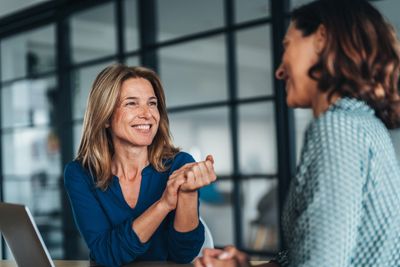Two women smiling and talking in an office setting.