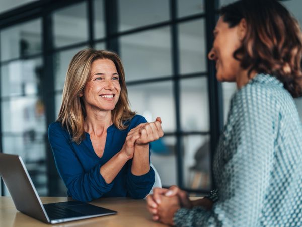 Two women having a friendly conversation at a desk with a laptop.