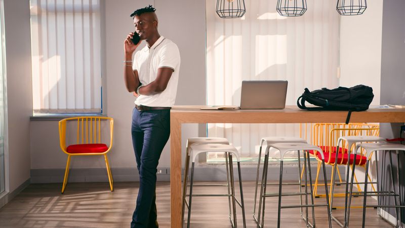 Brightly lit modern office featuring a tech savvy professional conversing on the phone. Elegant furniture decorates the space, reflecting a blend of style and functionality commonly seen in innovative workplaces.