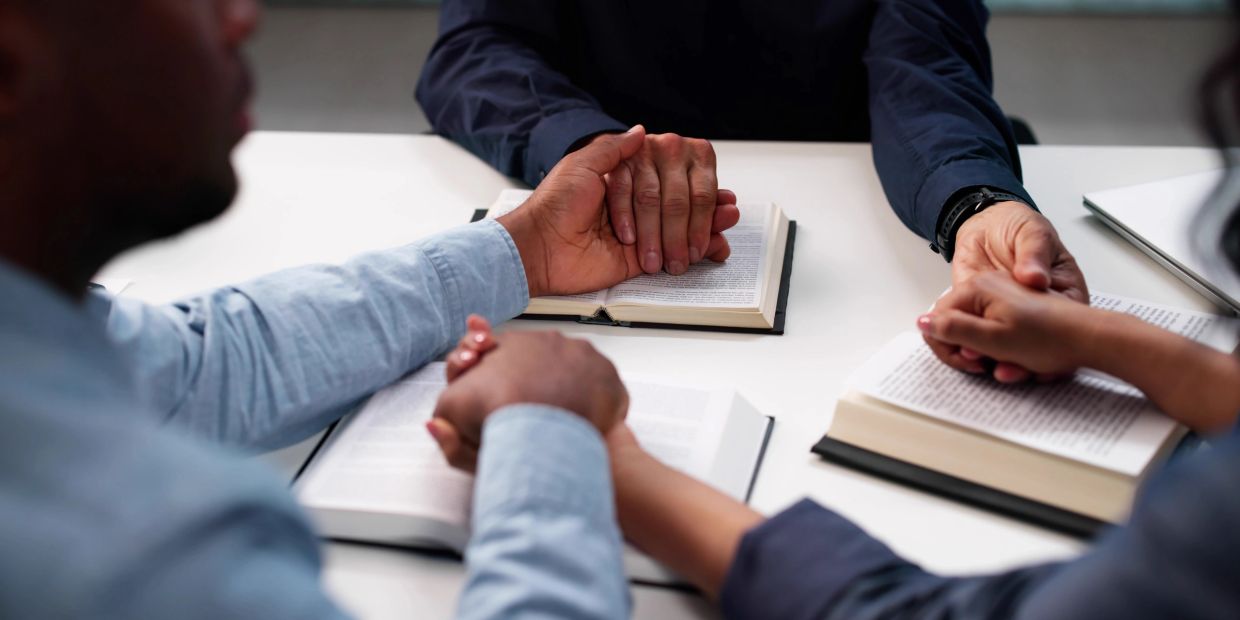 People holding hands over open books in prayer or support.