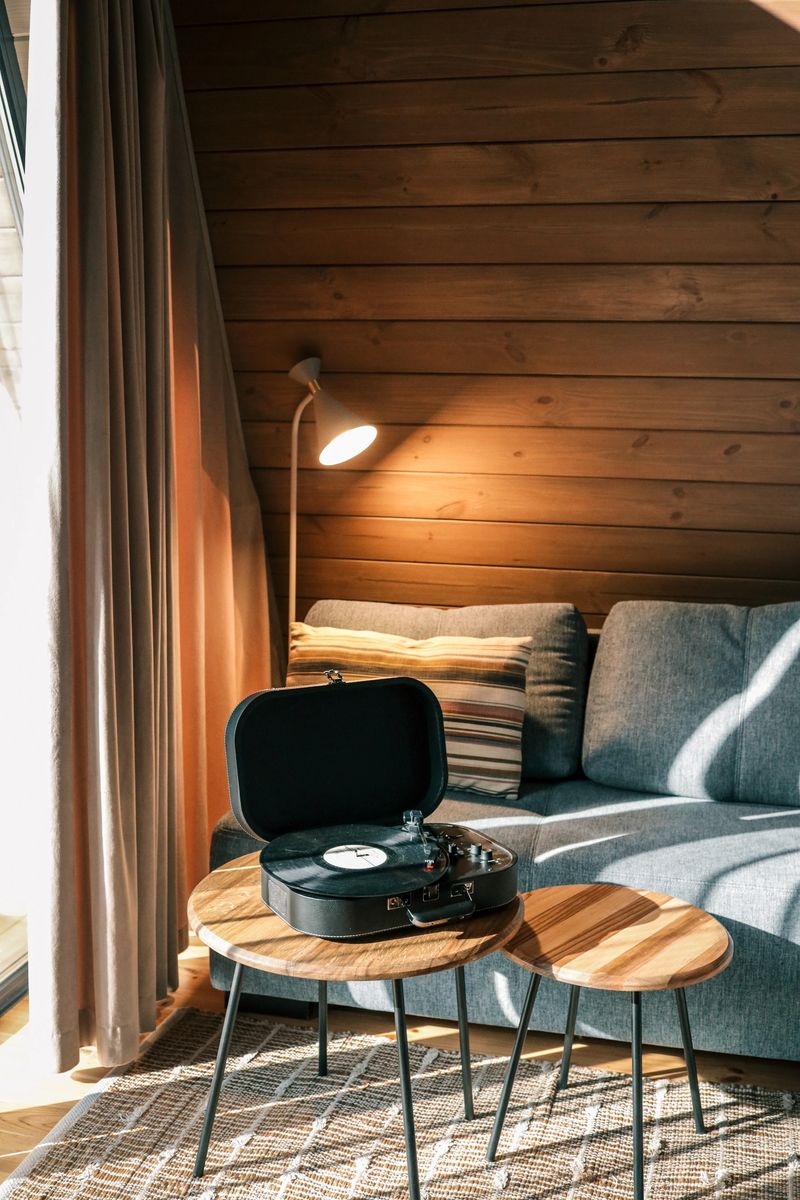 Turntable on a wooden coffee table in a cozy living room with soft lighting, striped pillow on a blue sofa, and warm wooden walls creating a calm retro atmosphere.