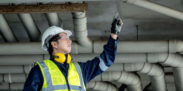 Engineer inspecting pipes in an industrial setting wearing safety gear.