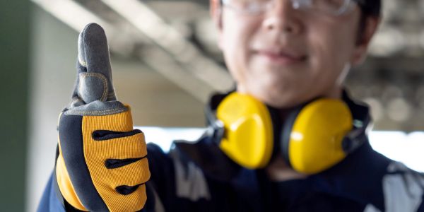 Person giving thumbs up with work gloves and ear protection.