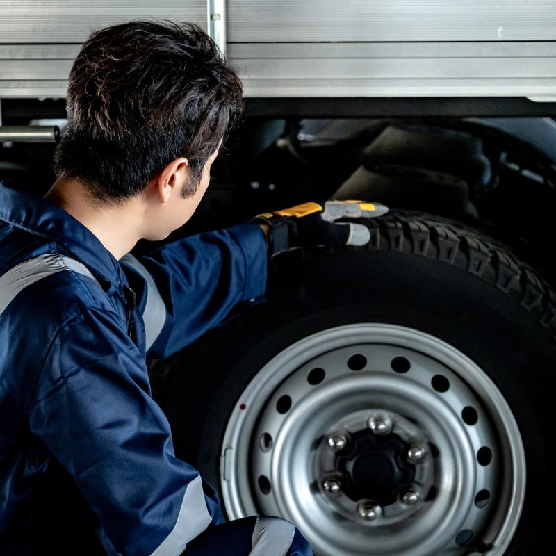 Tyre service and car suspension system maintenance for safety driving. Asian auto mechanic man checking car wheel and rubber tire tread in auto repair shop