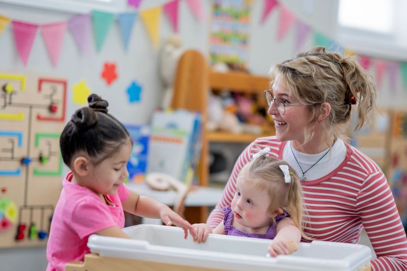 A cheerful preschool teacher interacts with two children, fostering learning and creativity in a vibrant educational setting.