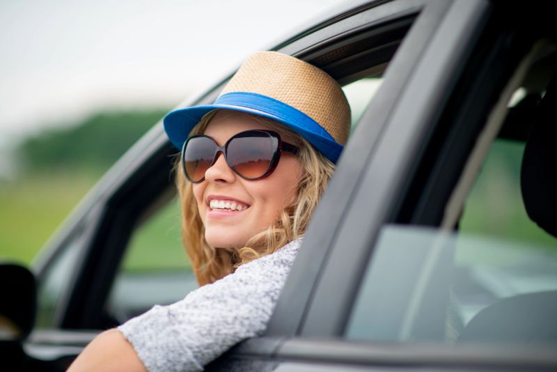 Blonde woman enjoying a relaxing road trip, smiling happily outdoors while sitting in her car.