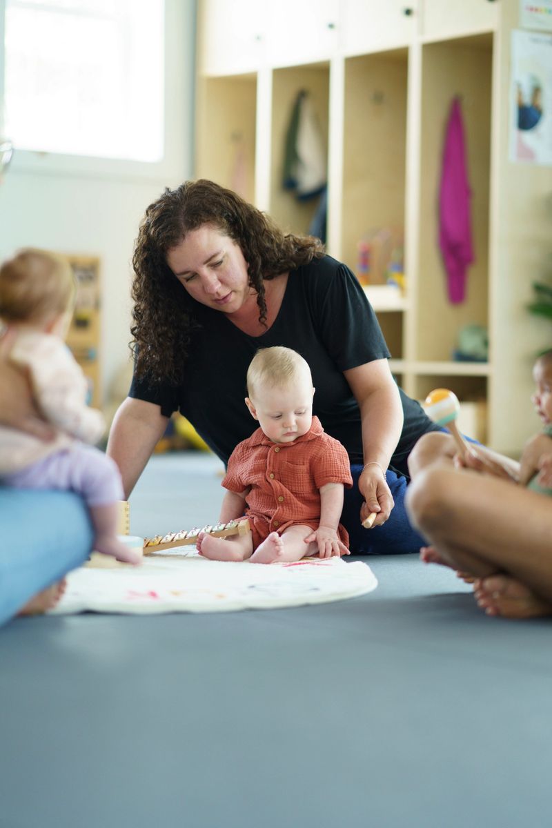 A thoughtful moment of a mother providing care and interaction with her baby at a daycare or playroom setting, fostering developmental growth and parenting engagement in an educational environment.