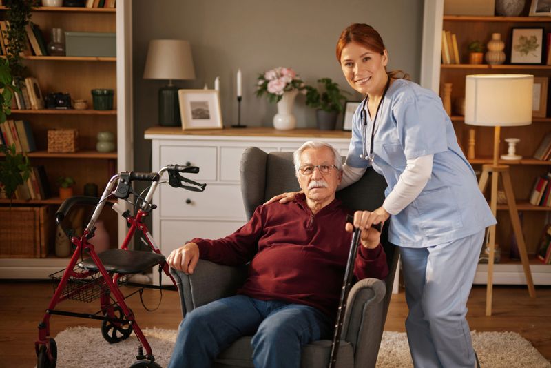Nurse smiling and assisting elderly man at home with walking cane and rollator