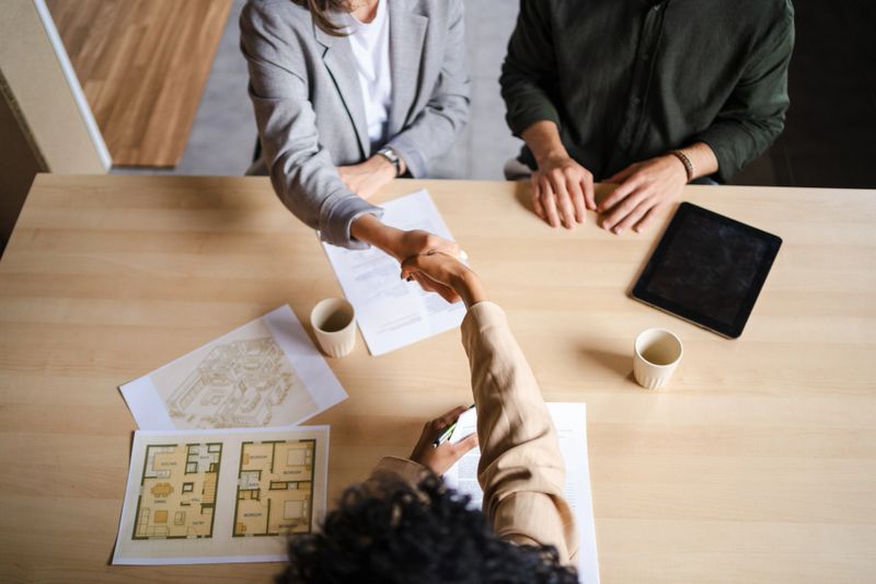 Professional architect greeting client, confirming project approval and examining architectural blueprints in modern office workspace