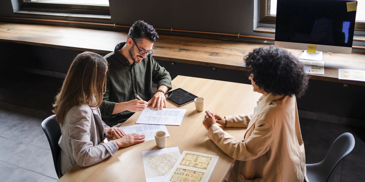 Three professionals reviewing documents at a wooden table in an office.