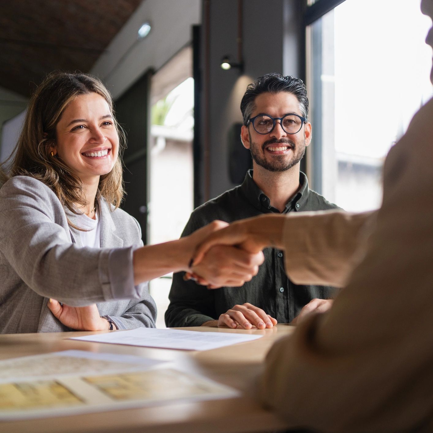 Smiling couple shaking hands with a third person in a professional setting.
