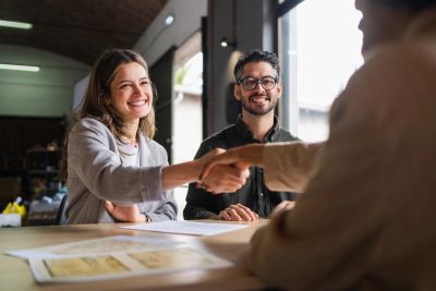 Two people smiling and shaking hands with a third person across a table.