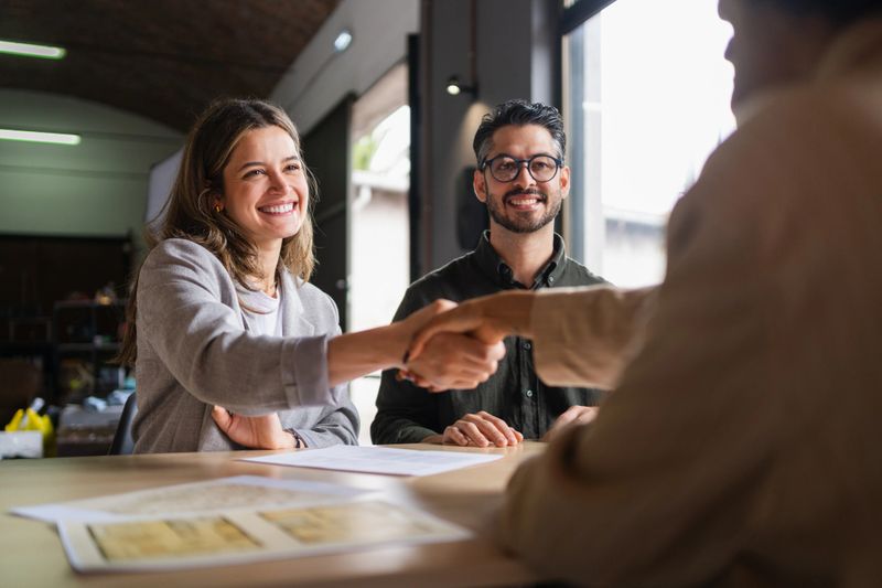 Business professionals greeting with firm handshake, confirming partnership and celebrating successful negotiation in modern corporate workspace