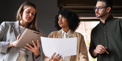 Three professionals discussing work documents and tablet in an office setting.