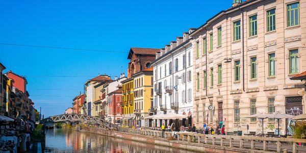 Colorful buildings line a calm canal under a clear blue sky with a small bridge in the distance.
