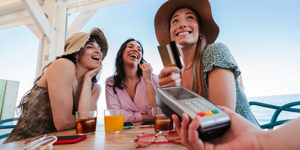Three women smiling with a credit card and payment terminal.