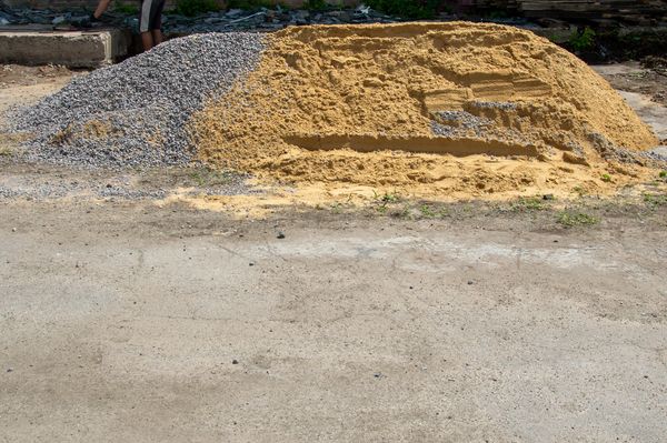 Piles of sand and gravel at a construction site with workers' legs visible.