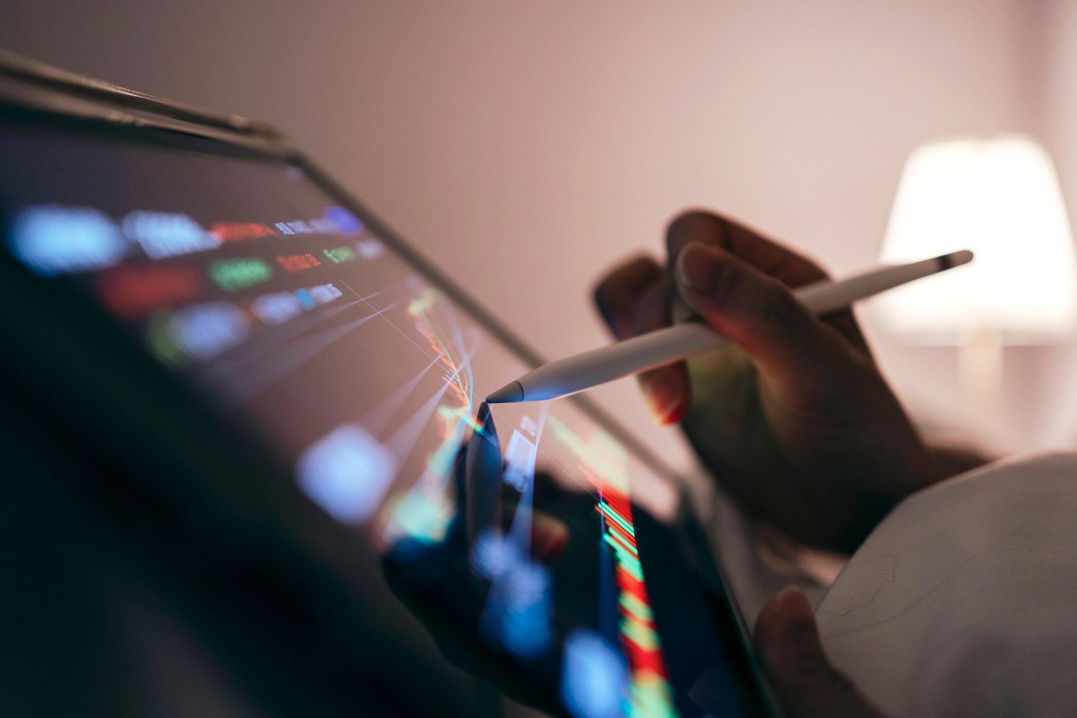 Hand using a stylus on a tablet displaying stock charts and data.
