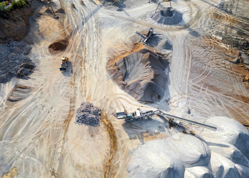 Overhead photograph of an active quarry site featuring industrial equipment, winding vehicle tracks, and distinct excavation areas amid piles of processed stone and mineral materials.