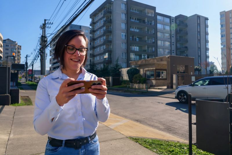 Young adult woman smiles while playing a mobile game on a city street
