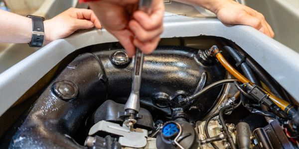 Hand using a socket wrench on machinery inside an engine compartment.