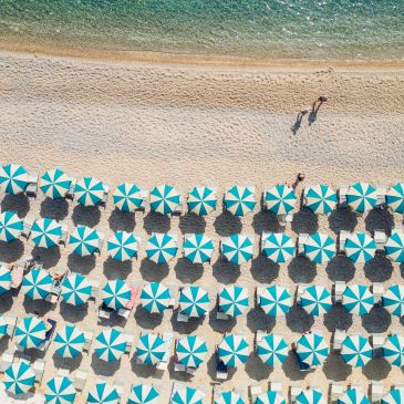 Aerial view of beach umbrellas and two people walking by the shore.