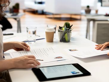 Two people reviewing resumes at a white office table with a tablet and coffee cup.