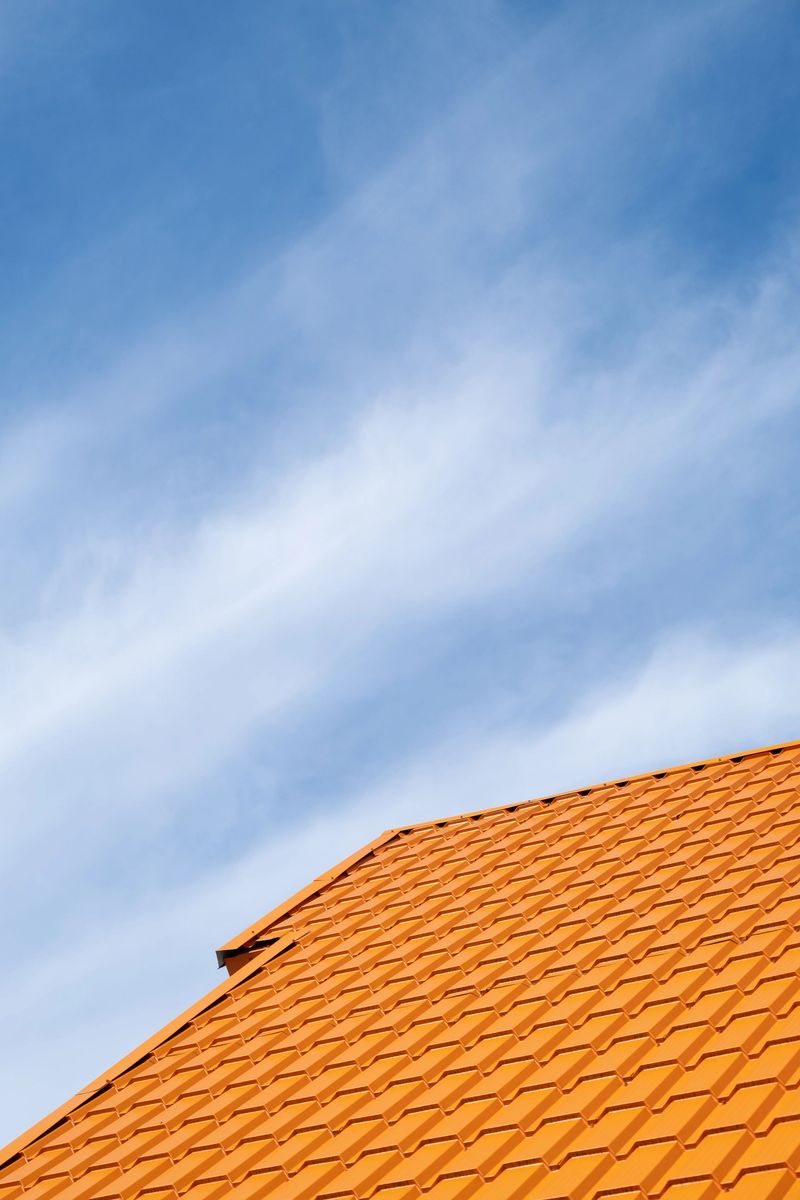 Bright orange roof of metal roofing tiles against blue sky background