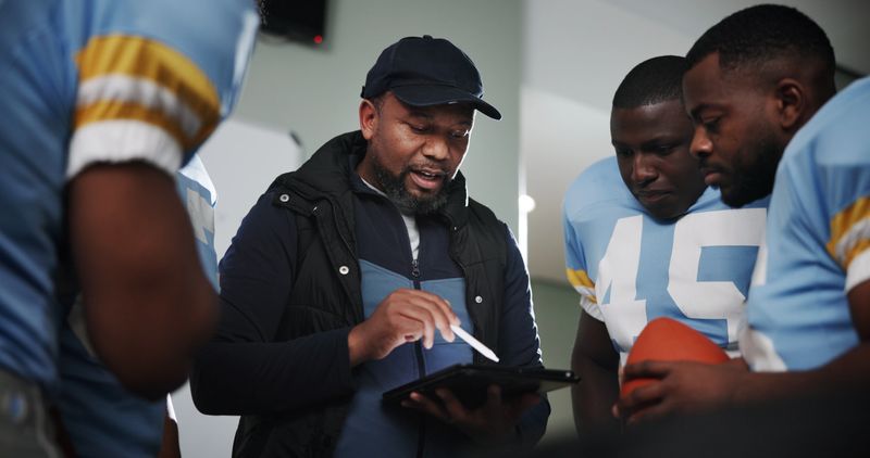 Tablet, coaching and football with team in locker room for game plan, sports strategy or defense formation. Touchdown tactics, match feedback and discussion with people and advice for training