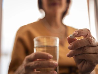 Person holding a white pill and a glass of water.