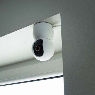 A white security camera mounted on a ceiling corner indoors.
