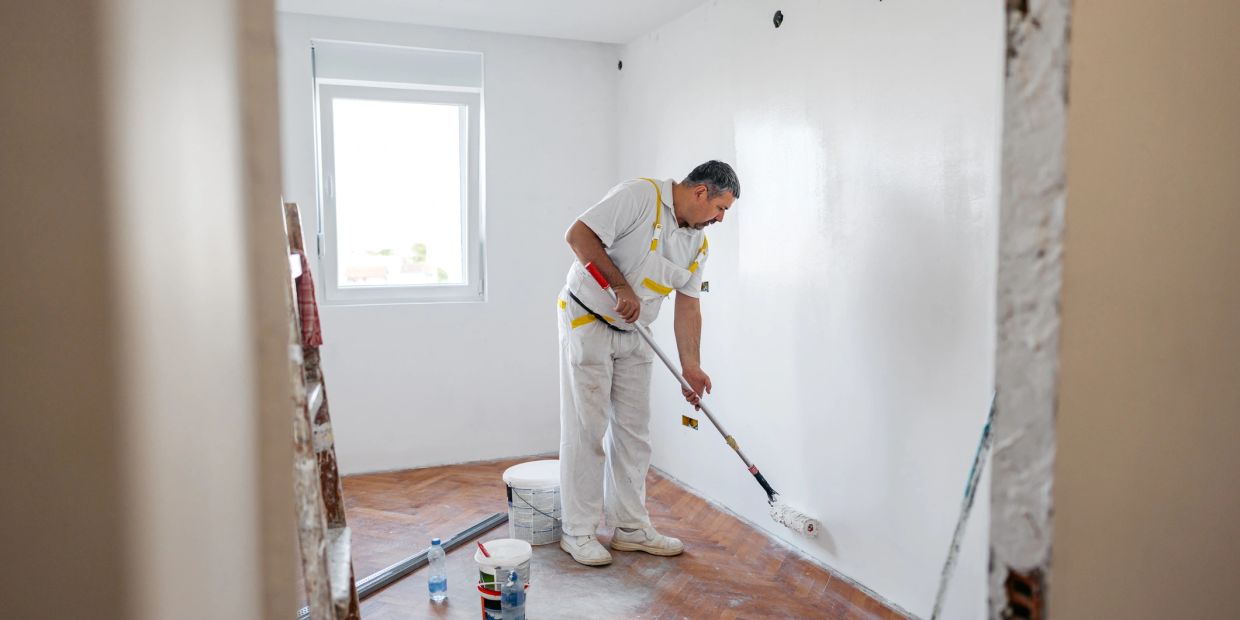 Man painting a white wall with a roller in a room.
