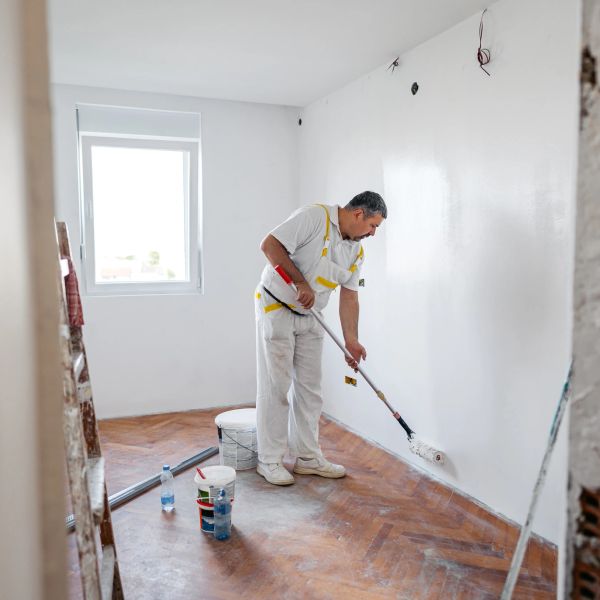 A man painting a white wall in a room.