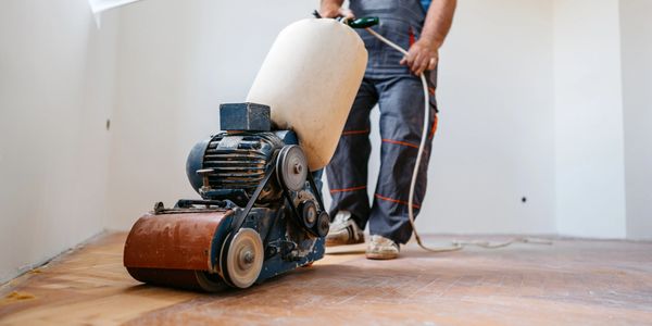 Worker using a floor sander on wooden floor.