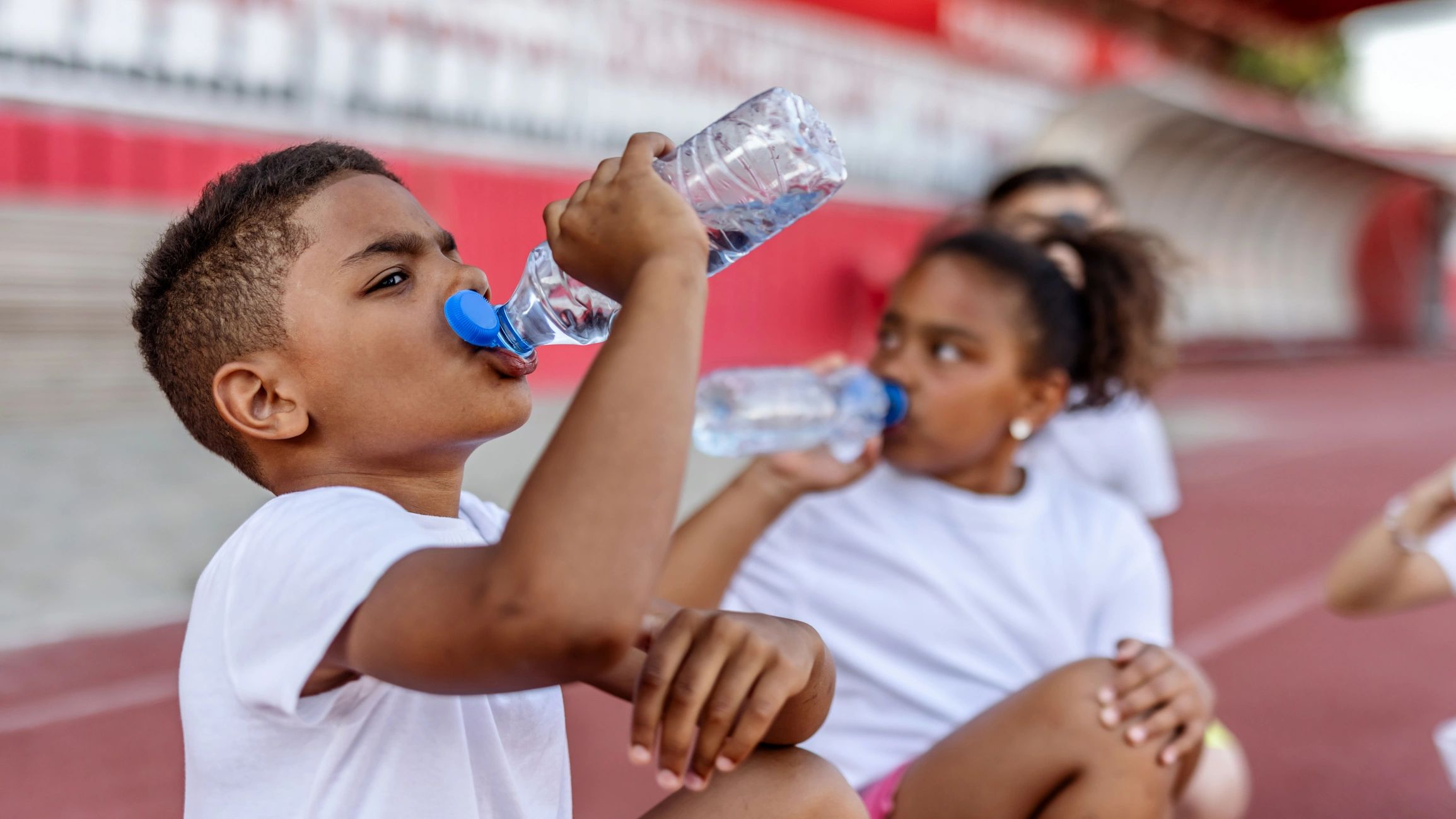 A boy and girl sitting on the track with their track club for practice.