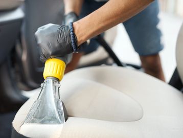 Person cleaning a car seat with a vacuum cleaner attachment.
