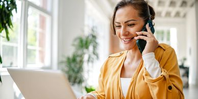 Woman talking on phone while using laptop.