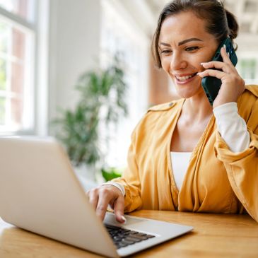 Woman working on laptop and talking on phone.