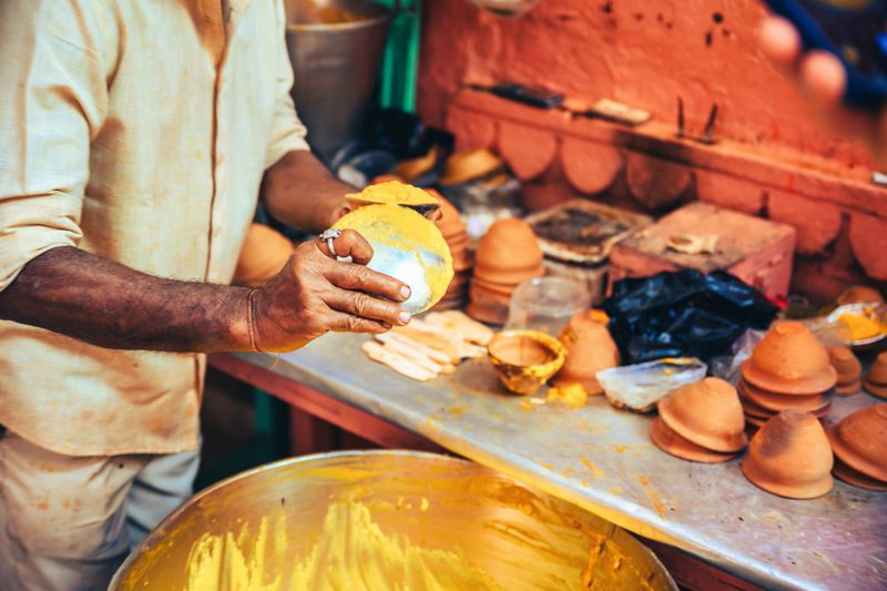 man putting out yellow sweet dessert from metal pan at food stall in Varanasi