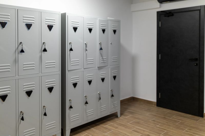 Grey metal lockers line the wall in a spacious locker room. The clean and organized area features a solid black door. Natural light illuminates the contemporary design.