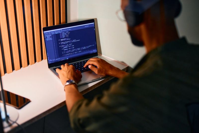 Focused computer programmer working on code using laptop in a modern office, developing software applications and innovative technology solutions