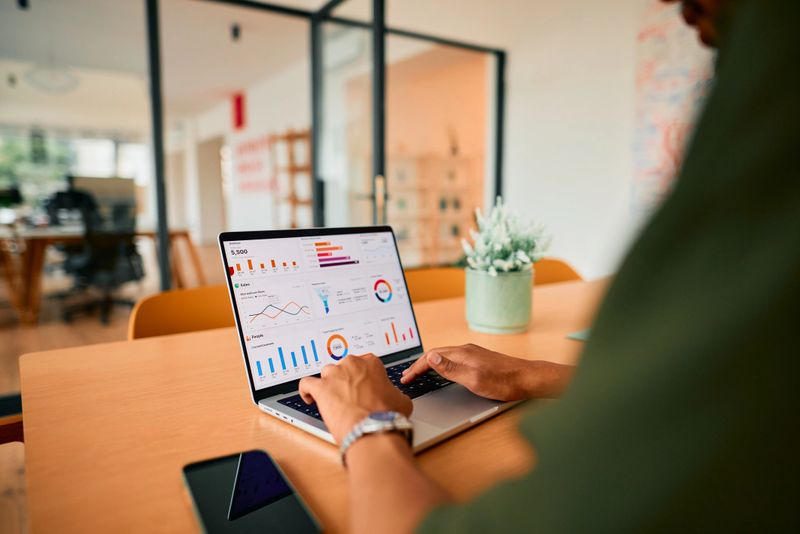 Businessman analyzing financial data on a laptop screen, focusing intently in a modern office environment. Charts and graphs illustrate key statistics and performance metrics