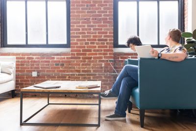 Two men sitting and working on laptops in a modern office with brick walls.