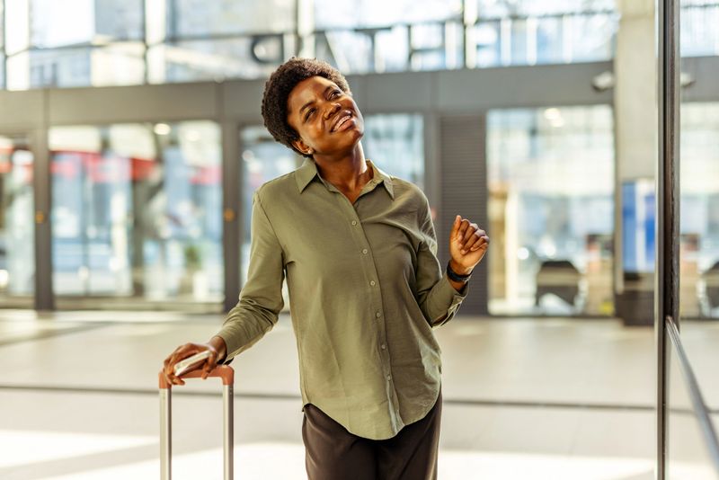 Smiling woman dressed casually with luggage, enjoying the journey inside a contemporary building with glass walls.