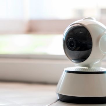 A white security camera on a tiled floor near a window.
