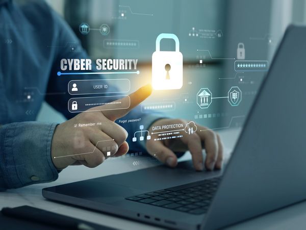 Person interacting with a laptop and cybersecurity holographic interface.