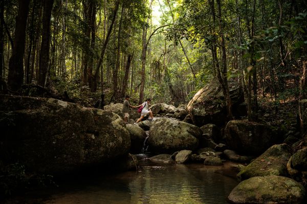 Hikers crossing rocks in a dense forest stream.