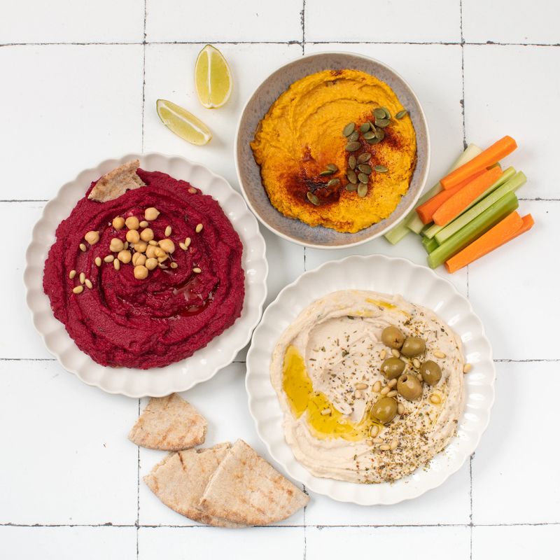 Different types of hummus in bowls and plates. Beetroot, pumpkin, chickpea and bean hummus. Healthy and vegetarian concept.
