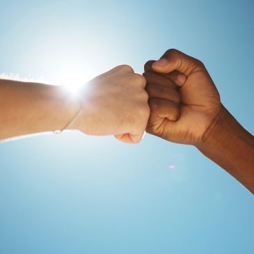 Two fists bumping under the bright sky.