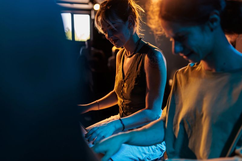 A male and female pianist perform a duet under vibrant blue and yellow stage lights, blending their talents to create a harmonious musical experience.